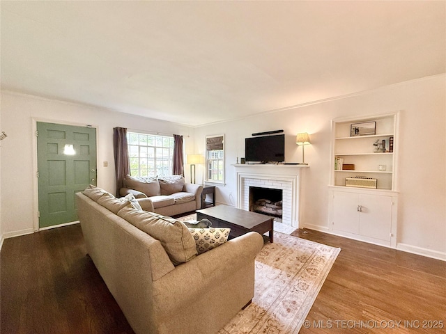 living area featuring built in shelves, dark wood finished floors, baseboards, and a fireplace