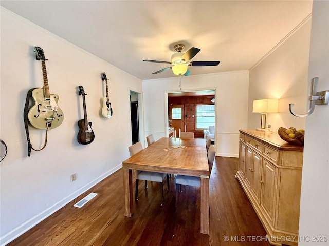 dining room featuring dark wood-style flooring, baseboards, crown molding, visible vents, and ceiling fan