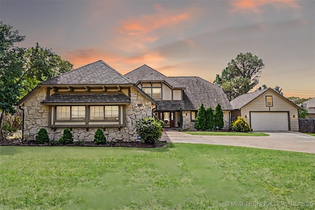 tudor home with concrete driveway, a front yard, stone siding, and an attached garage