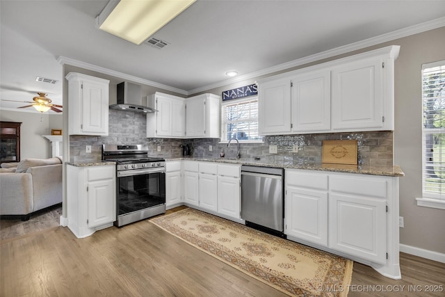 kitchen with visible vents, wall chimney exhaust hood, ceiling fan, appliances with stainless steel finishes, and light wood finished floors