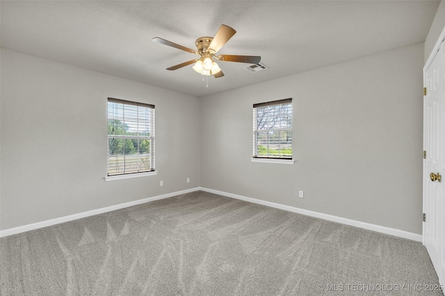 carpeted empty room featuring a wealth of natural light, visible vents, and baseboards