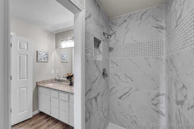 bathroom featuring a tile shower, wood finished floors, and vanity