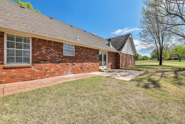 rear view of house with a patio area, brick siding, a yard, and roof with shingles