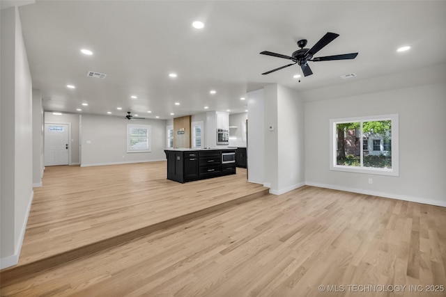 unfurnished living room featuring visible vents, baseboards, and ceiling fan