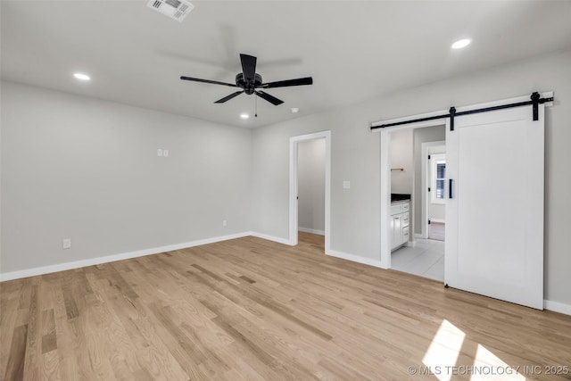 unfurnished bedroom featuring baseboards, recessed lighting, a barn door, light wood-style floors, and visible vents
