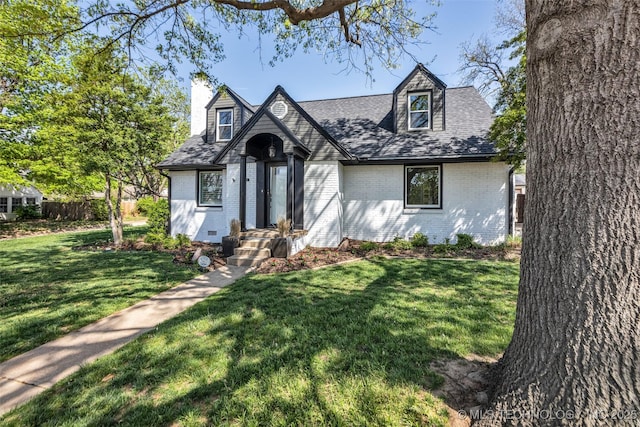 tudor house with roof with shingles, brick siding, a chimney, and a front lawn