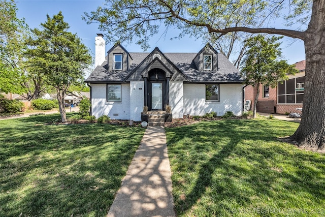 view of front of property featuring brick siding, a front yard, roof with shingles, and a chimney