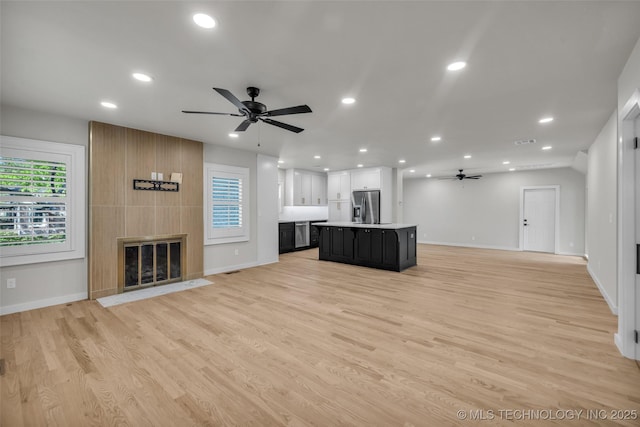 unfurnished living room with light wood-style flooring, baseboards, and ceiling fan