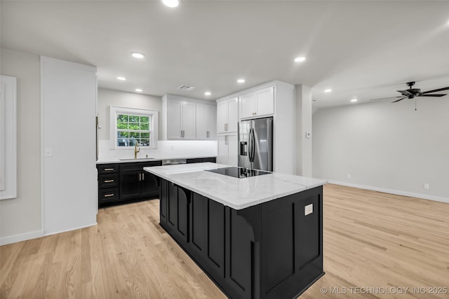 kitchen featuring dark cabinets, white cabinetry, a sink, stainless steel fridge, and black electric cooktop