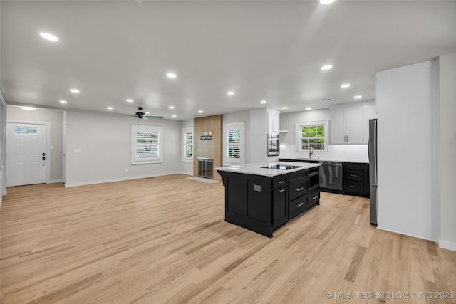 kitchen with dark cabinets, recessed lighting, light wood-style flooring, a center island, and appliances with stainless steel finishes