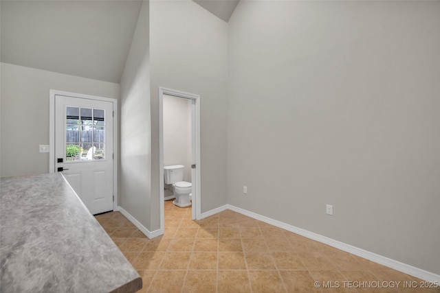 foyer entrance featuring light tile patterned floors, baseboards, and high vaulted ceiling