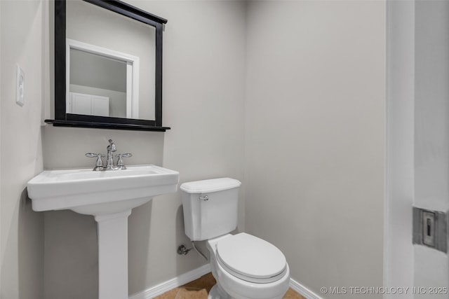 half bathroom with toilet, baseboards, and a sink