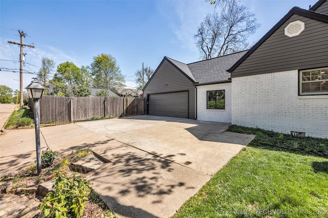 view of home's exterior with concrete driveway, roof with shingles, brick siding, a garage, and fence
