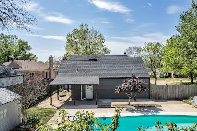 rear view of house with roof with shingles, a patio area, a fenced in pool, and fence
