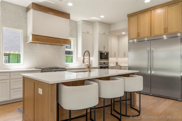 17822 E Patriot Dr, Owasso, OK 74055 - kitchen with built in appliances, a kitchen island with sink, light wood-type flooring, decorative backsplash, and a breakfast bar area