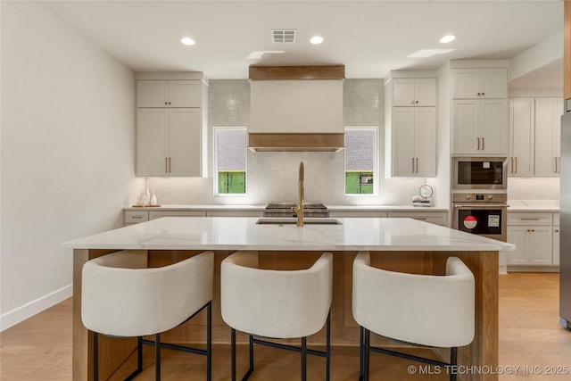 17822 E Patriot Dr, Owasso, OK 74055 - kitchen featuring stainless steel oven, built in microwave, an island with sink, premium range hood, and a kitchen breakfast bar