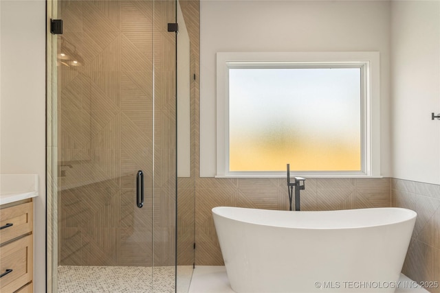 17822 E Patriot Dr, Owasso, OK 74055 - bathroom featuring tile walls, a soaking tub, a shower stall, vanity, and a wainscoted wall