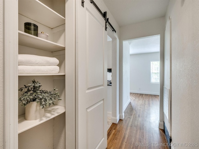 hallway with a barn door, baseboards, and wood finished floors