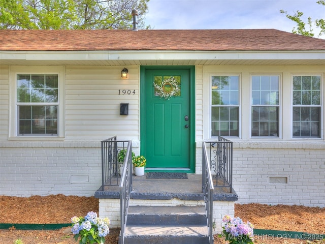 entrance to property featuring crawl space, a shingled roof, and brick siding