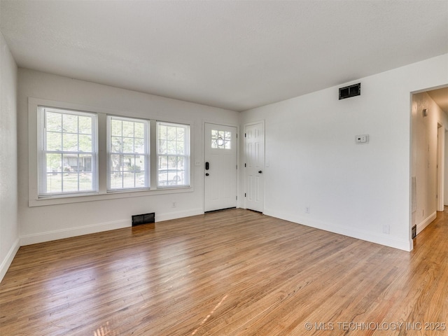 unfurnished living room featuring baseboards, visible vents, and light wood-style floors