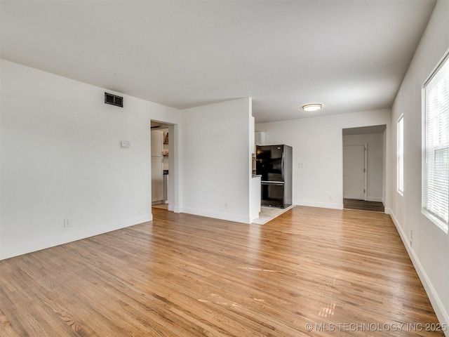 unfurnished living room featuring light wood-style floors, visible vents, and baseboards