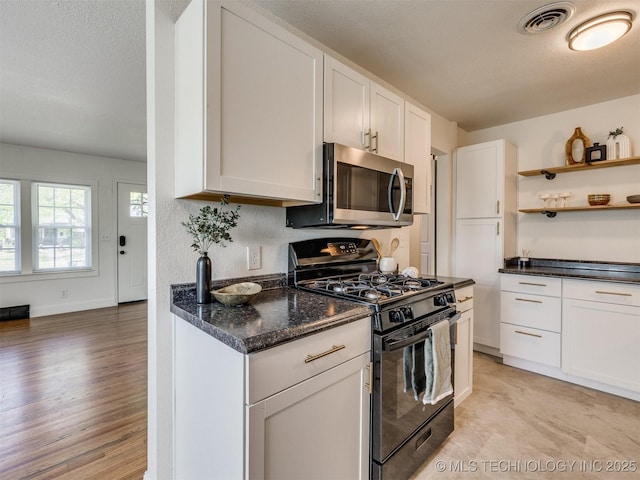 kitchen with dark stone countertops, stainless steel microwave, visible vents, black gas range, and white cabinetry