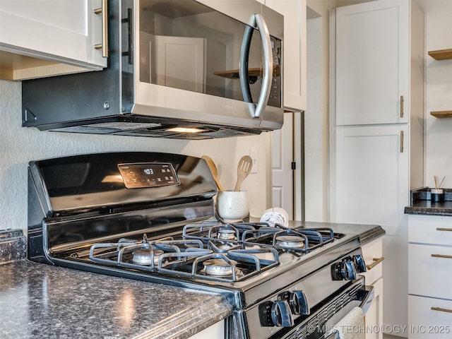 kitchen featuring stainless steel microwave, range with gas cooktop, dark stone countertops, and white cabinets