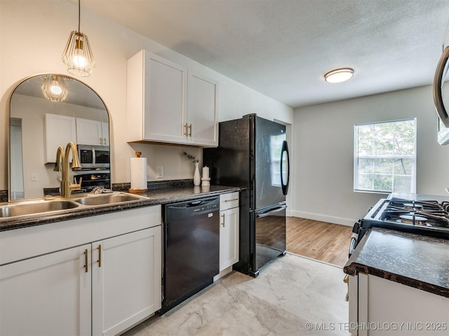 kitchen featuring dark countertops, a sink, black appliances, hanging light fixtures, and white cabinetry