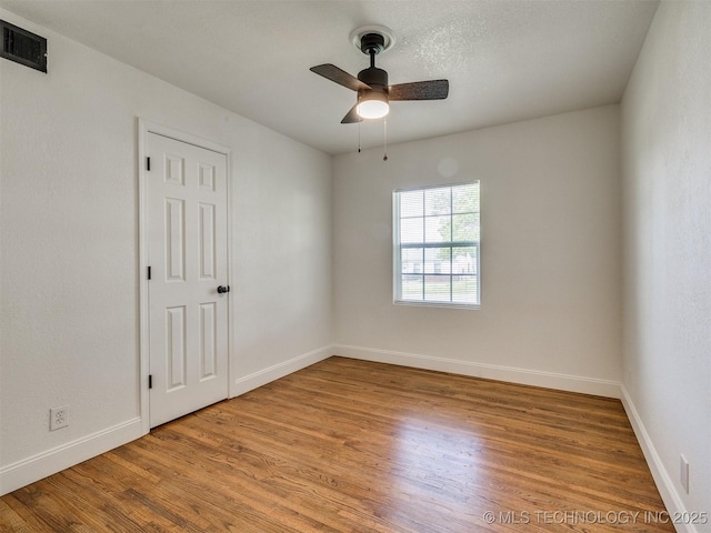 spare room featuring baseboards, a ceiling fan, wood finished floors, and visible vents