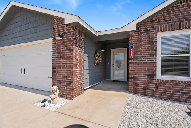 doorway to property with a garage, concrete driveway, and brick siding
