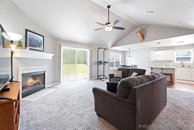 living room with ceiling fan, lofted ceiling with beams, a fireplace with flush hearth, visible vents, and light carpet