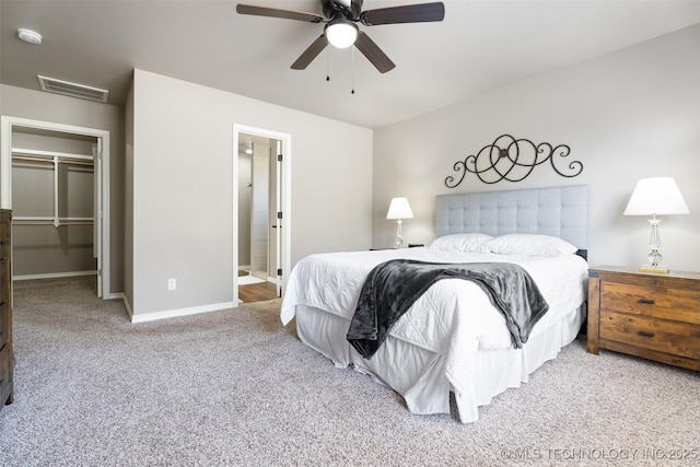 carpeted bedroom featuring ensuite bathroom, a ceiling fan, visible vents, a walk in closet, and baseboards