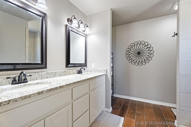 bathroom with a sink, baseboards, double vanity, and wood finished floors