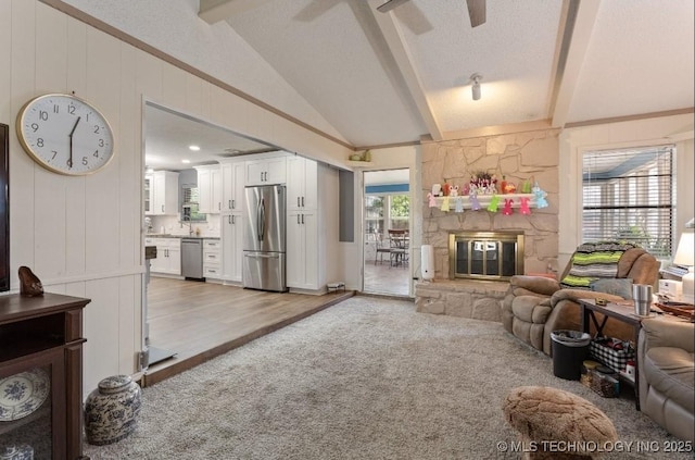 living room with vaulted ceiling with beams, a decorative wall, a fireplace, light colored carpet, and ceiling fan