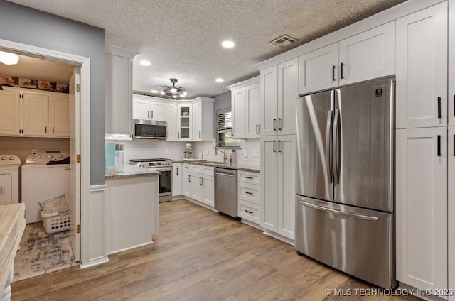 kitchen with a textured ceiling, stainless steel appliances, white cabinetry, visible vents, and independent washer and dryer