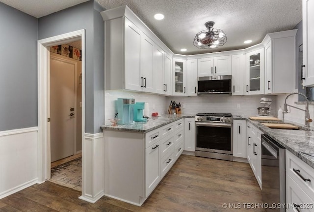 kitchen with tasteful backsplash, a sink, stainless steel appliances, white cabinets, and dark wood-style flooring