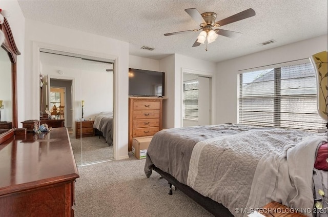 bedroom with a textured ceiling, multiple closets, light colored carpet, and visible vents