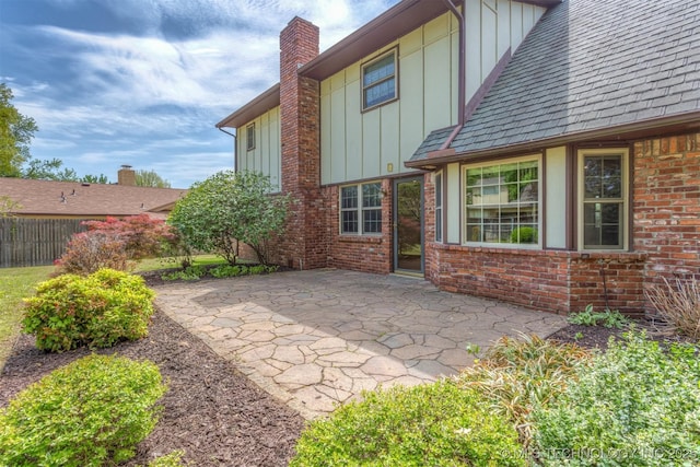 rear view of property featuring a chimney, board and batten siding, brick siding, fence, and a patio area