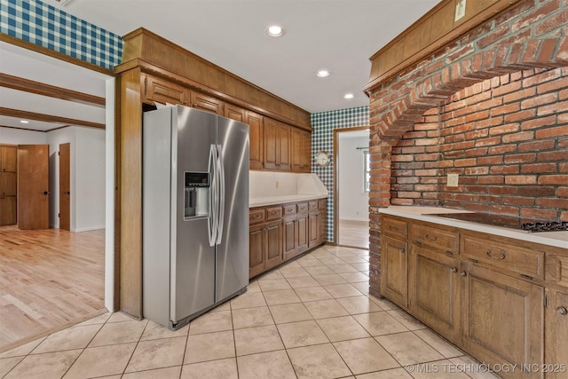 kitchen with stainless steel fridge with ice dispenser, light tile patterned flooring, black electric stovetop, and brick wall