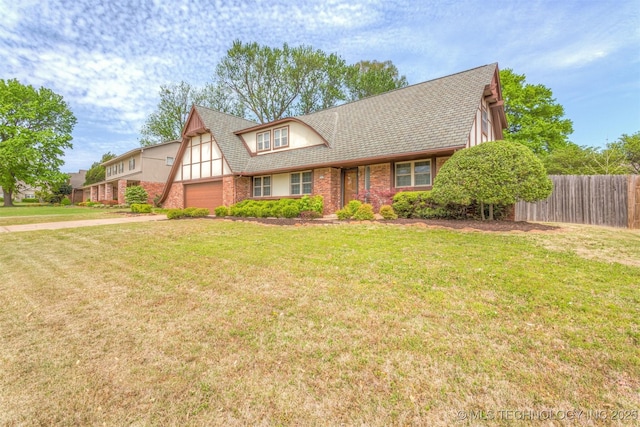 tudor house featuring a front yard, brick siding, an attached garage, and fence