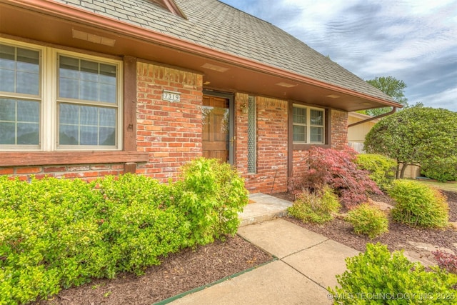 entrance to property featuring a shingled roof, brick siding, and a porch