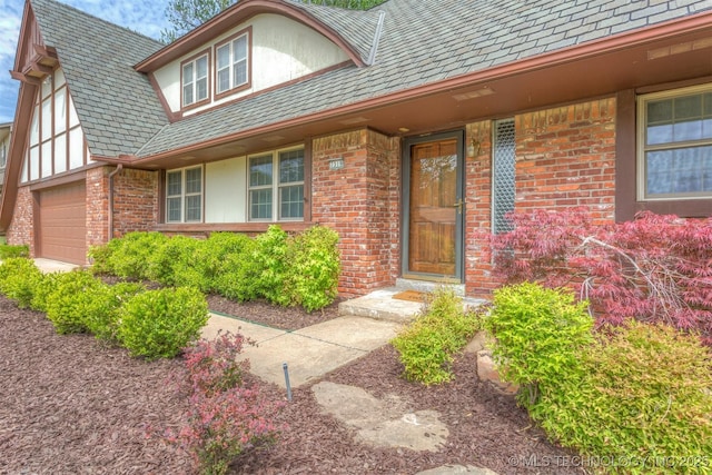 property entrance with stucco siding, an attached garage, a high end roof, and brick siding