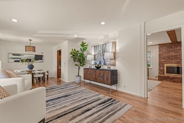 living area with wood finished floors, baseboards, a brick fireplace, and recessed lighting