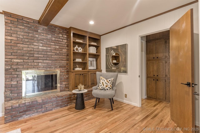 living area featuring beam ceiling, a fireplace, light wood finished floors, crown molding, and baseboards