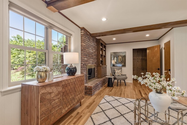 living area with ornamental molding, beamed ceiling, light wood-style flooring, and a healthy amount of sunlight