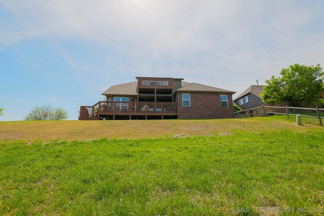 rear view of property featuring fence, a wooden deck, brick siding, and a yard