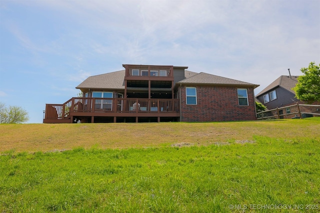 back of property with a lawn, roof with shingles, brick siding, and a deck