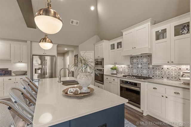 kitchen featuring appliances with stainless steel finishes, a sink, light countertops, a kitchen island with sink, and decorative backsplash
