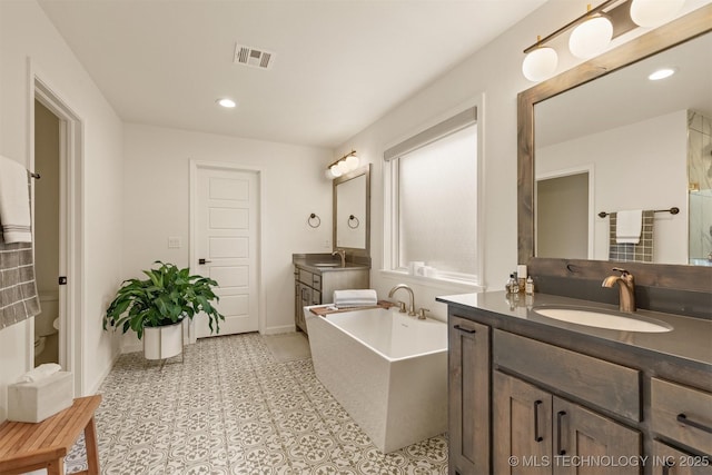 full bath with a freestanding tub, two vanities, baseboards, toilet, and recessed lighting