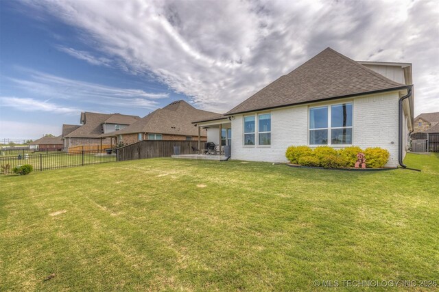 rear view of property featuring central AC unit, a shingled roof, brick siding, and a patio area